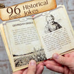 Open book with illustrations and text, held by a person against a rustic background.