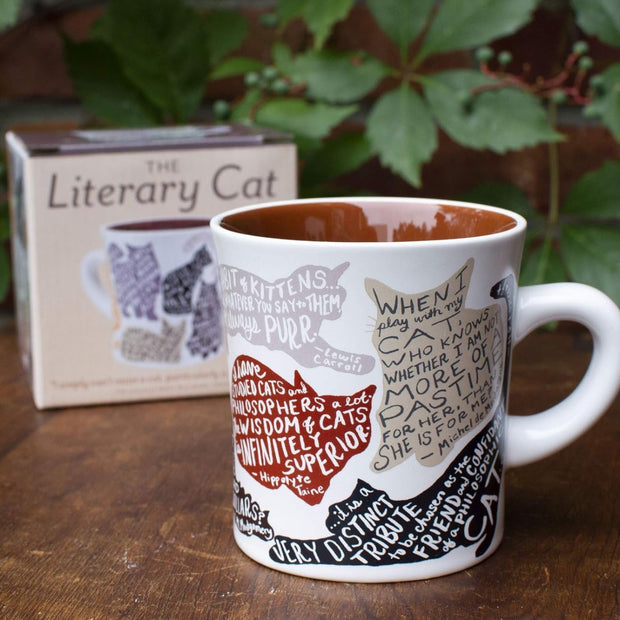 Mug with cat-themed design on a wooden surface with a box labeled 'The Literary Cat' in the background.