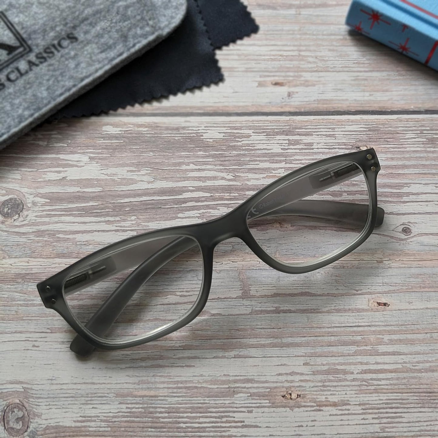 Black eyeglasses on a wooden surface with a cloth and box in the background.