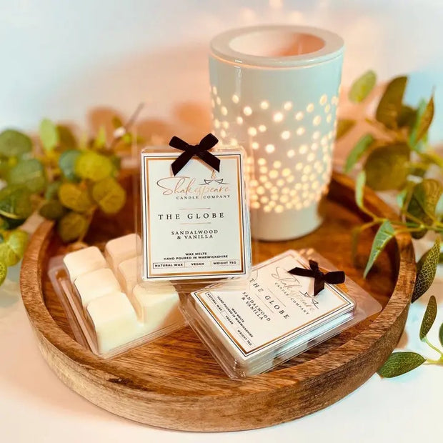 The Globe Wax Melts on a tray on a table with a lit candle and leaves in the background.