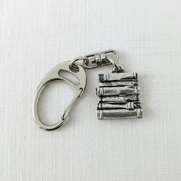 A silver metal keychain featuring a carabiner clip and a charm shaped like a stack of five books, displayed on a grey textured background.